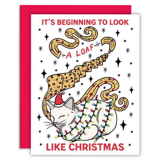 A white cat with a christmas santa hat wrapped in holiday lights in a loaf position with a fruitcake loaf and decorative text that says it’s looking a loaf like christmas