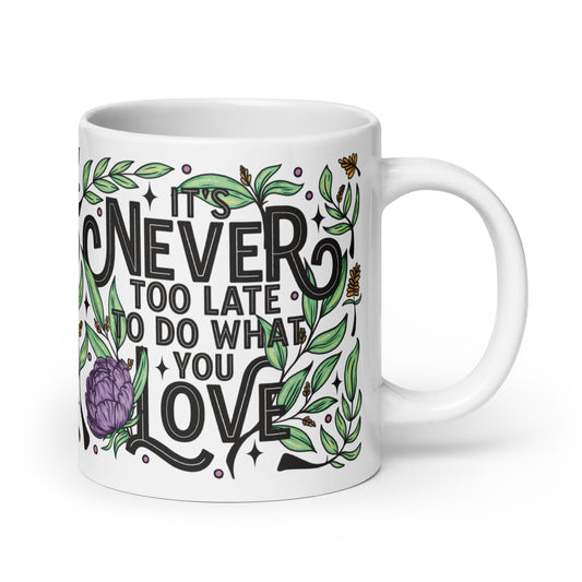 Decorative text that says ‘it’s never too late to do what you love’ in black, with floral decoration and stars surrounding printed on a white ceramic mug.